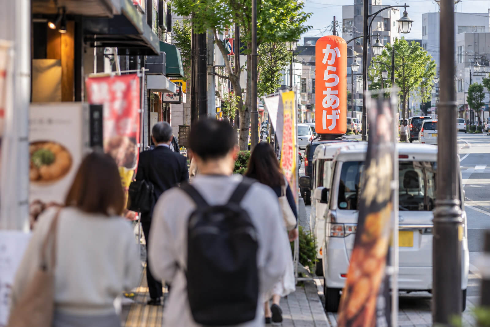 歩行者の目線から見た商店街。駐車車両やのぼり旗の上に、高さ3mのエアー看板の上半分がはっきり見えている