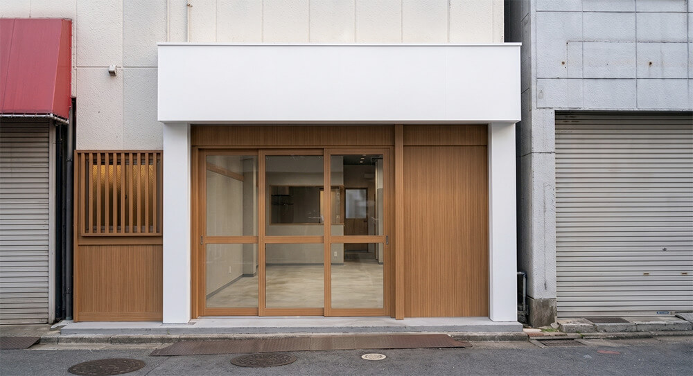 「酒場 萬屋」様の看板製作前（ビフォー）の店舗外観。看板のない白い袖壁と木目調ファサードの状態。