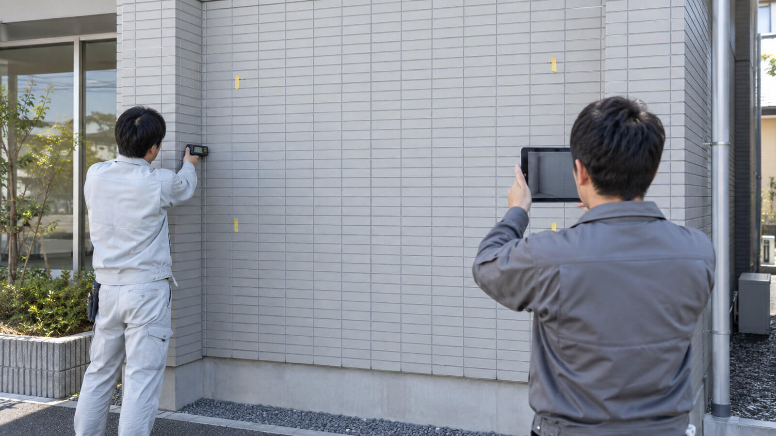 施工スタッフが会社の外壁の幅と高さをレーザー距離計で測り、看板の位置を確認している様子