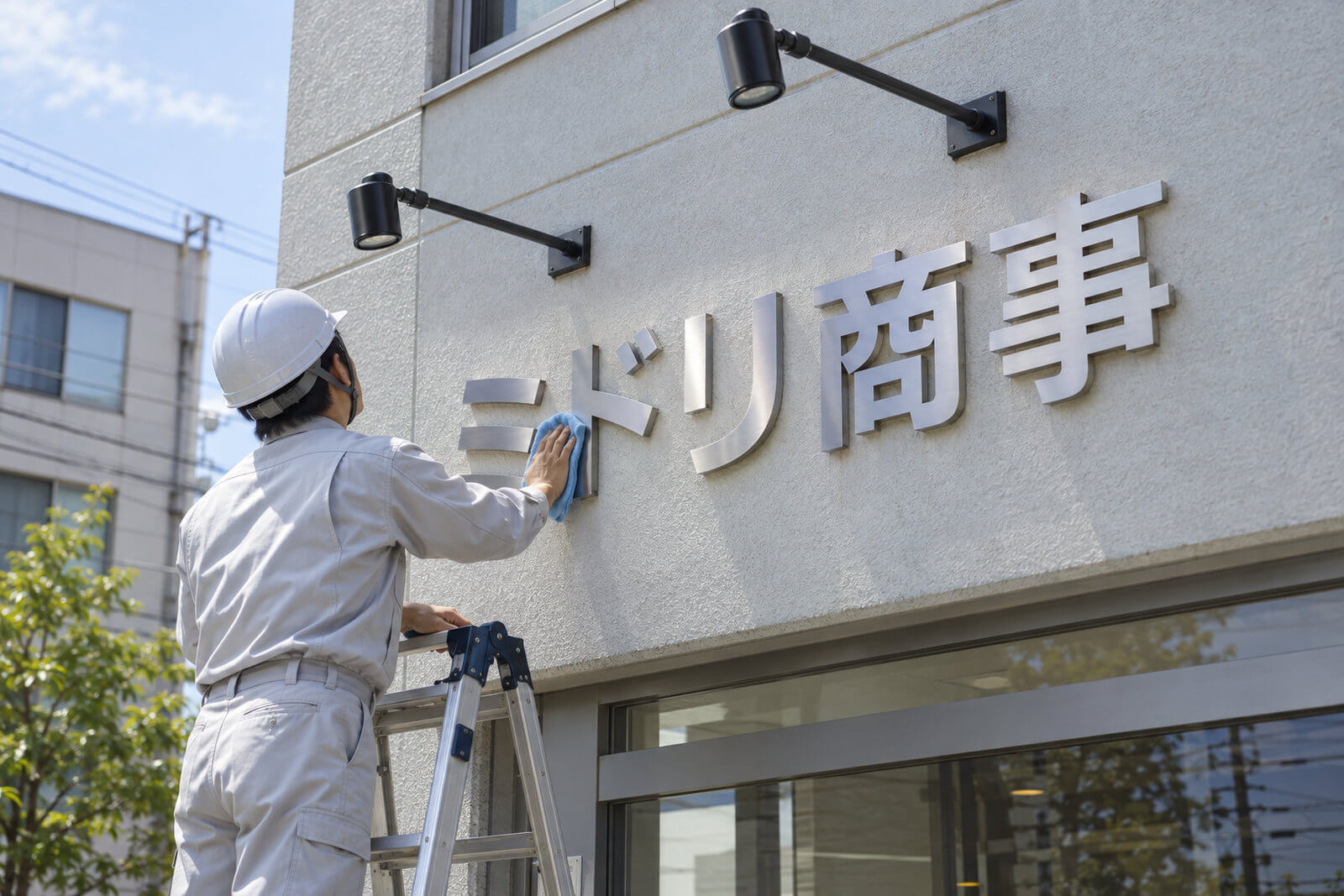 施工スタッフが会社外壁のステンレス切文字とスポットライトを点検・清掃している様子
