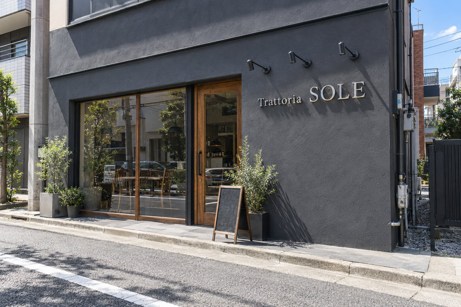 昼間の店舗外壁に浮かし取付したステンレス切文字とアームスポットライト