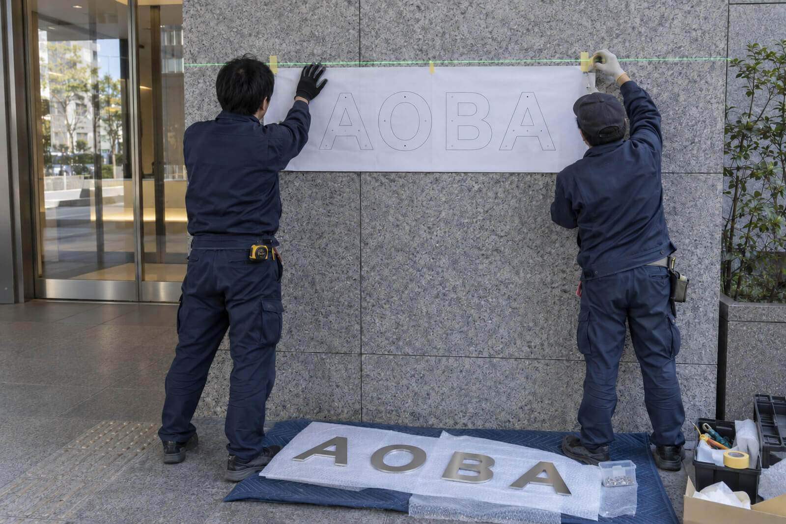 施工スタッフが原寸テンプレートを壁に貼って切文字の取付位置を決めている様子