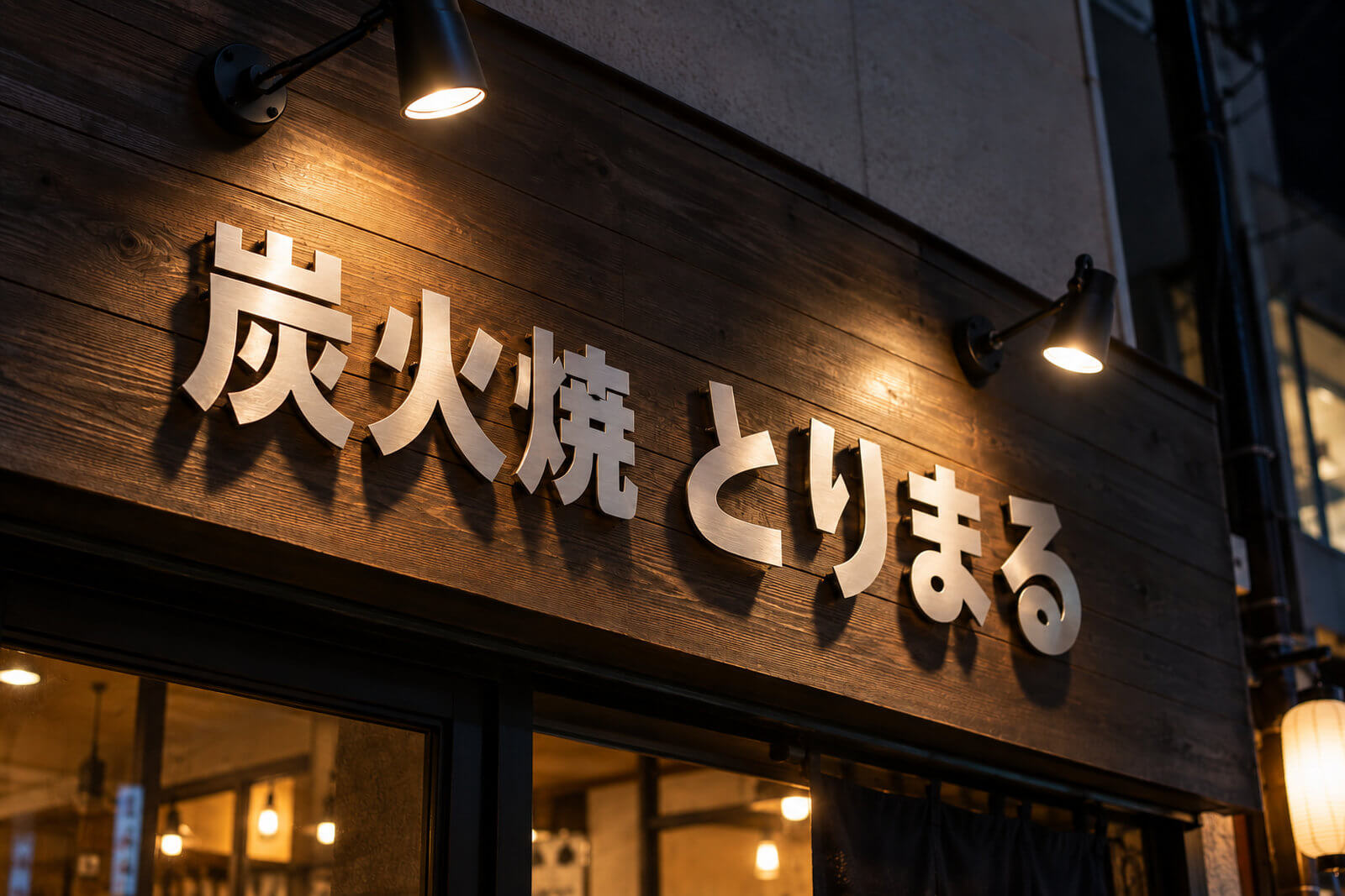 夜の店舗外壁で浮かし取付したステンレス切文字をスポットライトが照らし影が伸びている様子