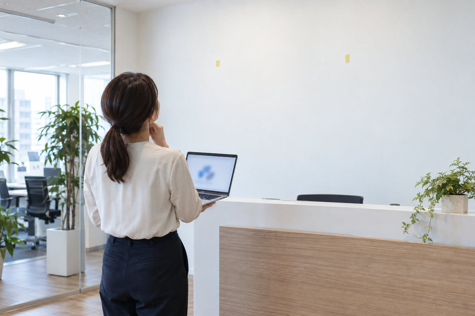 オフィスの白い壁の前でロゴデータを表示したノートパソコンを見ながら看板を検討する担当者