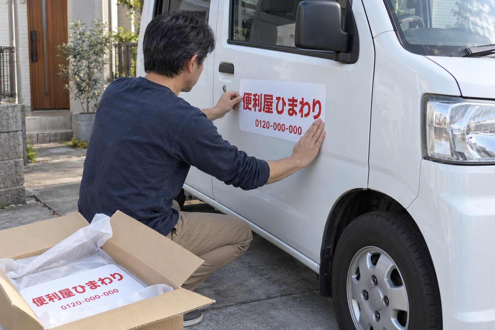 届いた箱から取り出した社名入りマグネット看板を、営業車のドアに端から貼っている手元