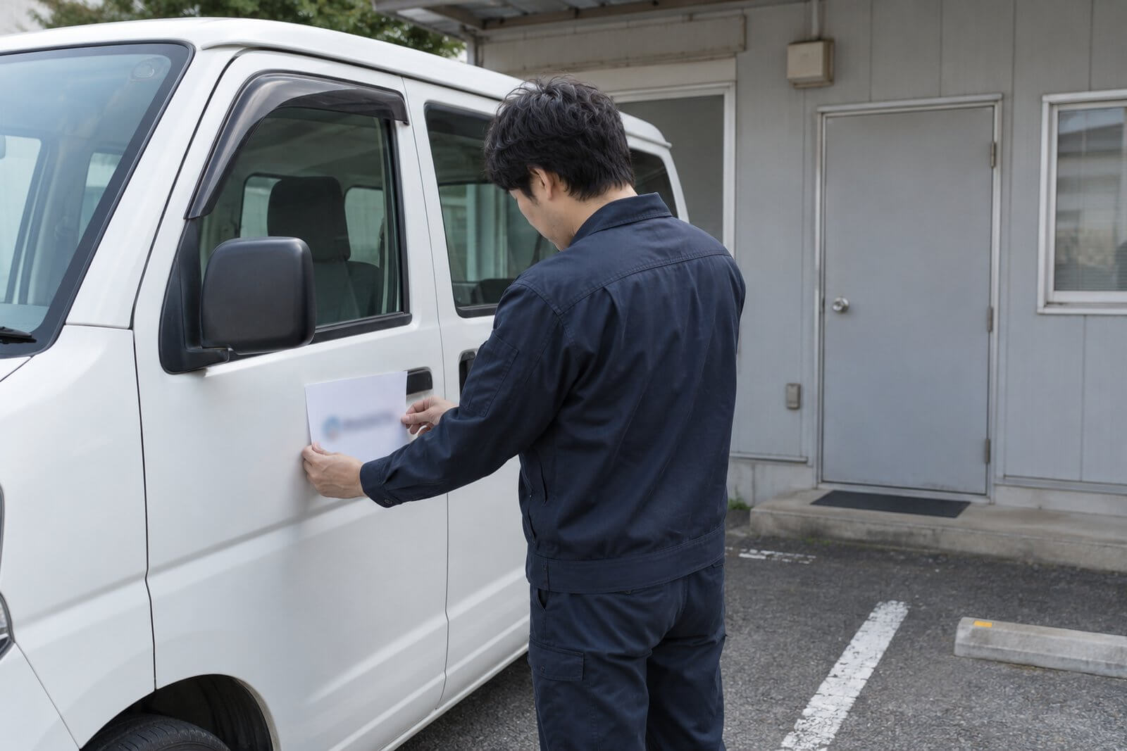 社用車のドアと事務所の鉄扉を前に、どこに社名を出すか悩む担当者
