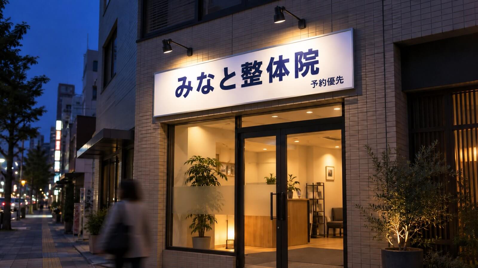 夕方の店舗入口の上に取り付けたアルミ複合板のファサード看板と、それを照らすアームスポットライト