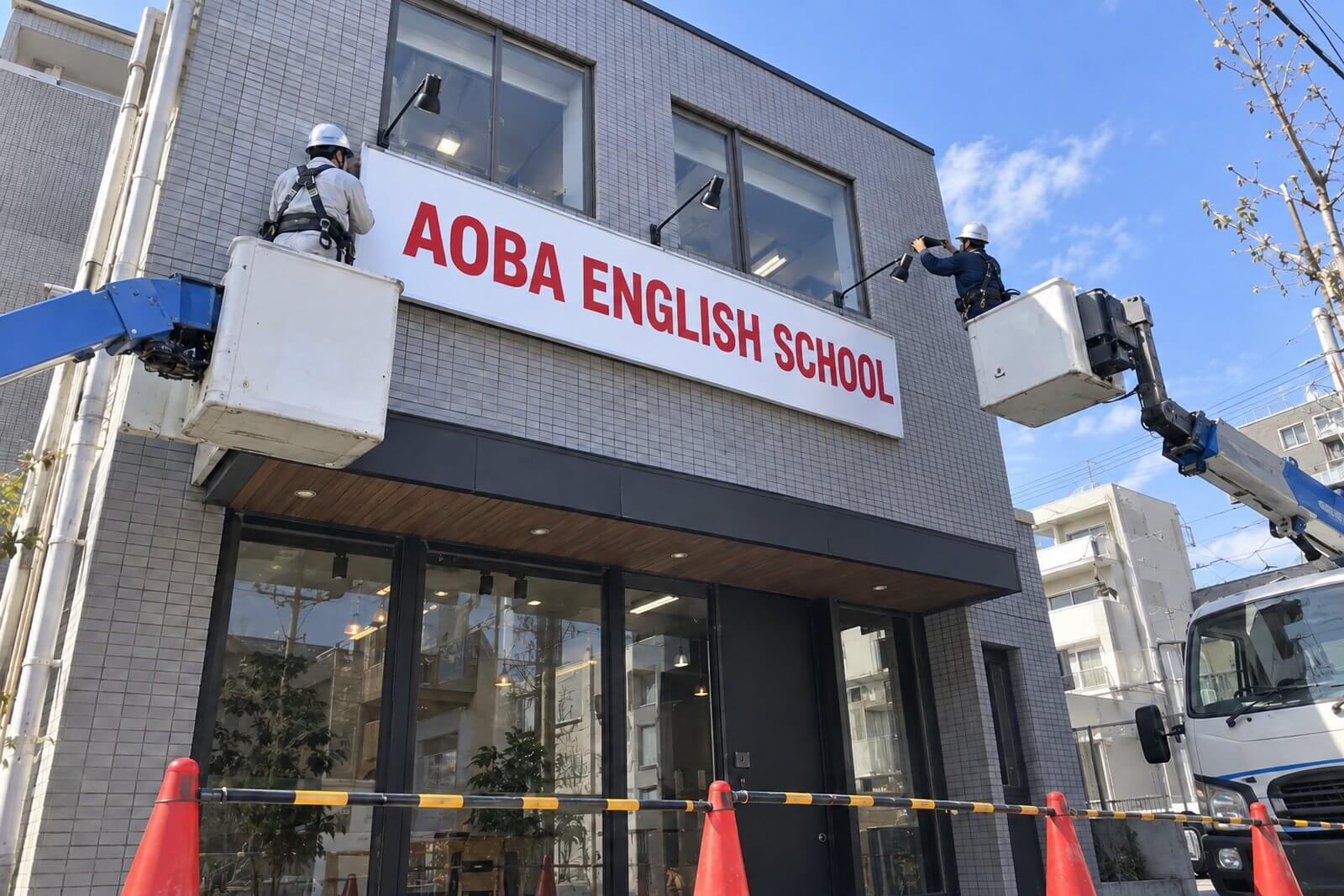 施工スタッフが高所作業車から店舗外壁にアルミ枠付きの大型プレート看板とスポットライトを取り付けている様子
