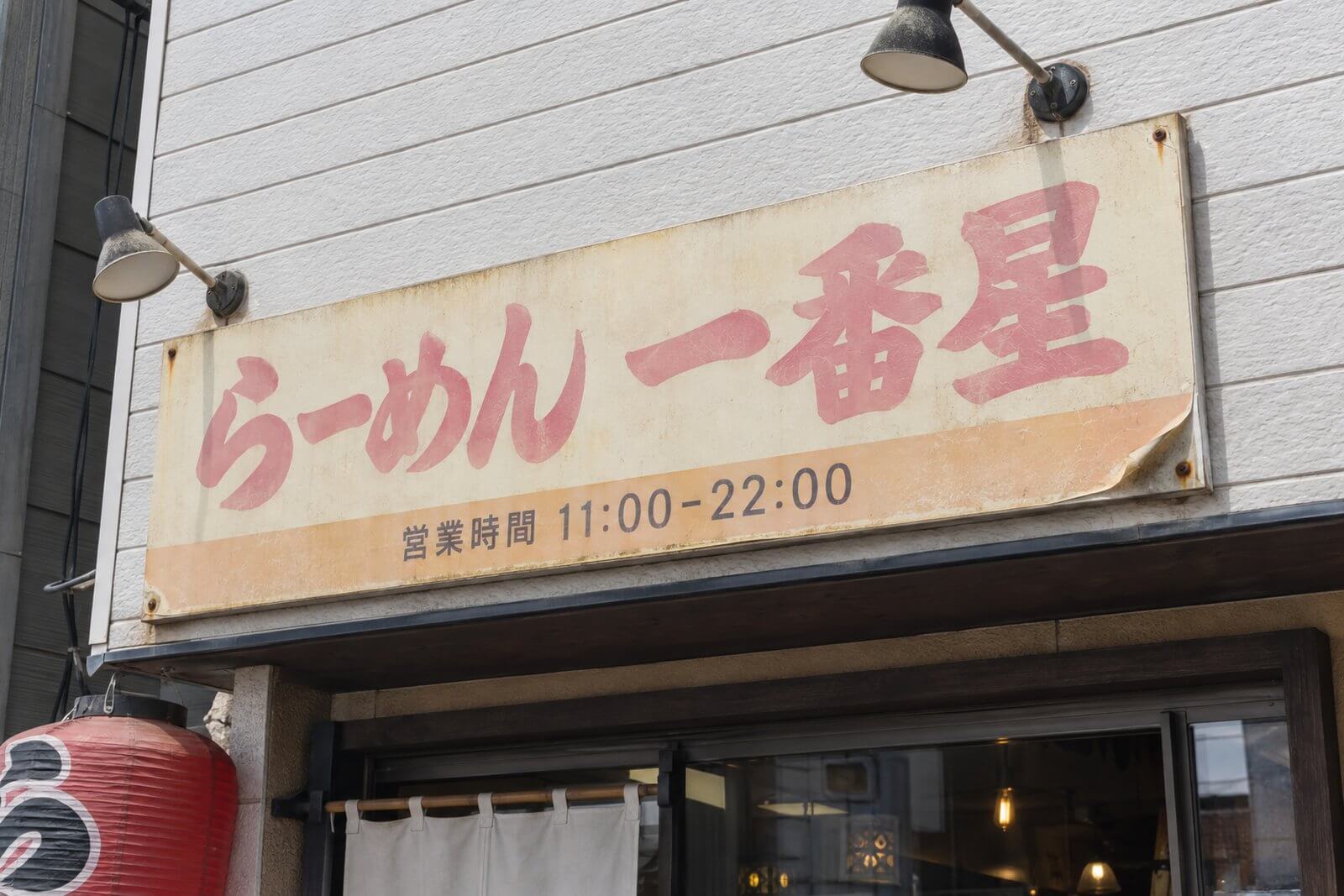 長年の直射日光で赤が薄くなり白が黄ばみ、端がめくれた店舗のプレート看板