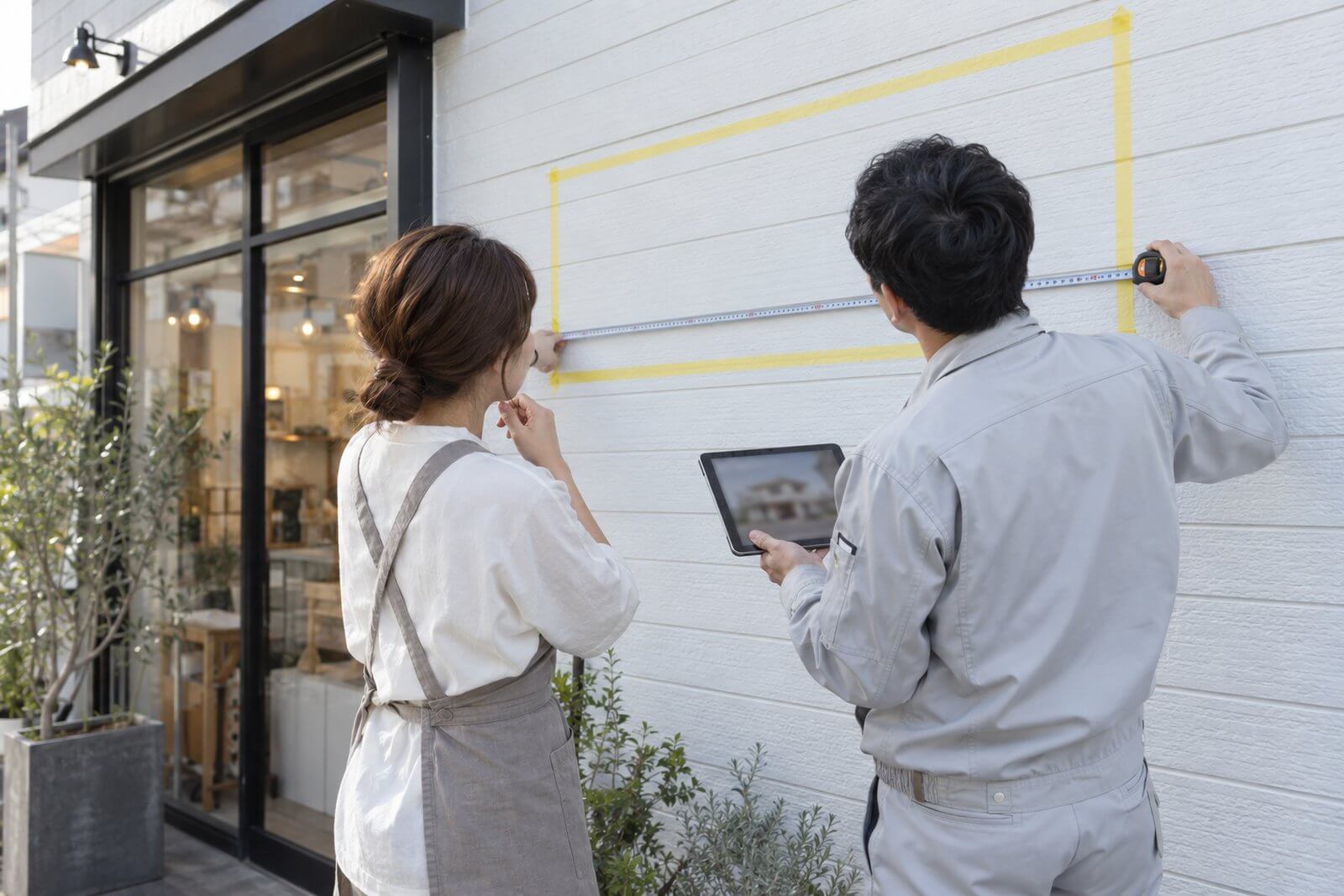 店舗の外壁の前で、看板のサイズと取付位置を相談する店舗オーナーと担当者