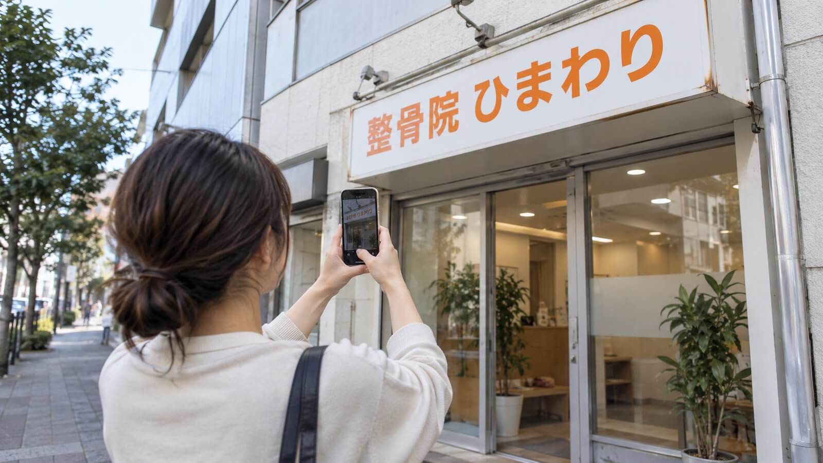店舗の前でスマートフォンを構え、壁面看板の全景と取付部を撮影して送ろうとしている担当者