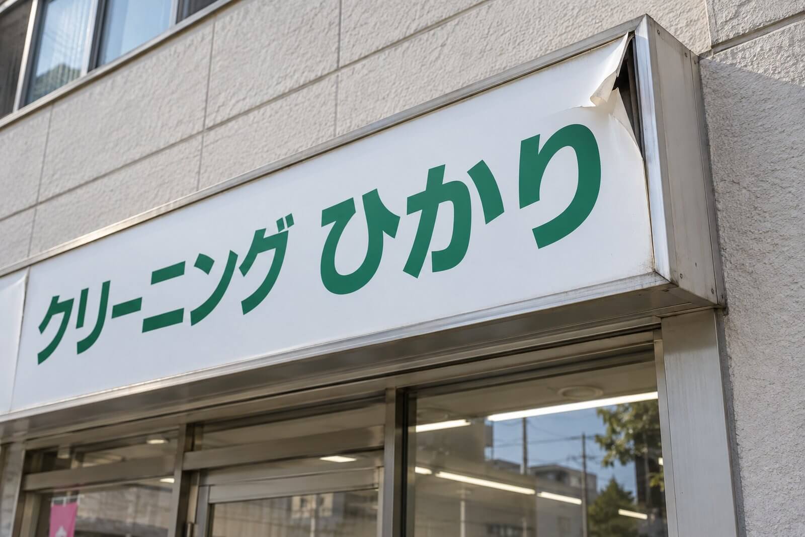 壁面看板のアルミ複合板の面板が角から剥がれて浮き、風でめくれかけている様子