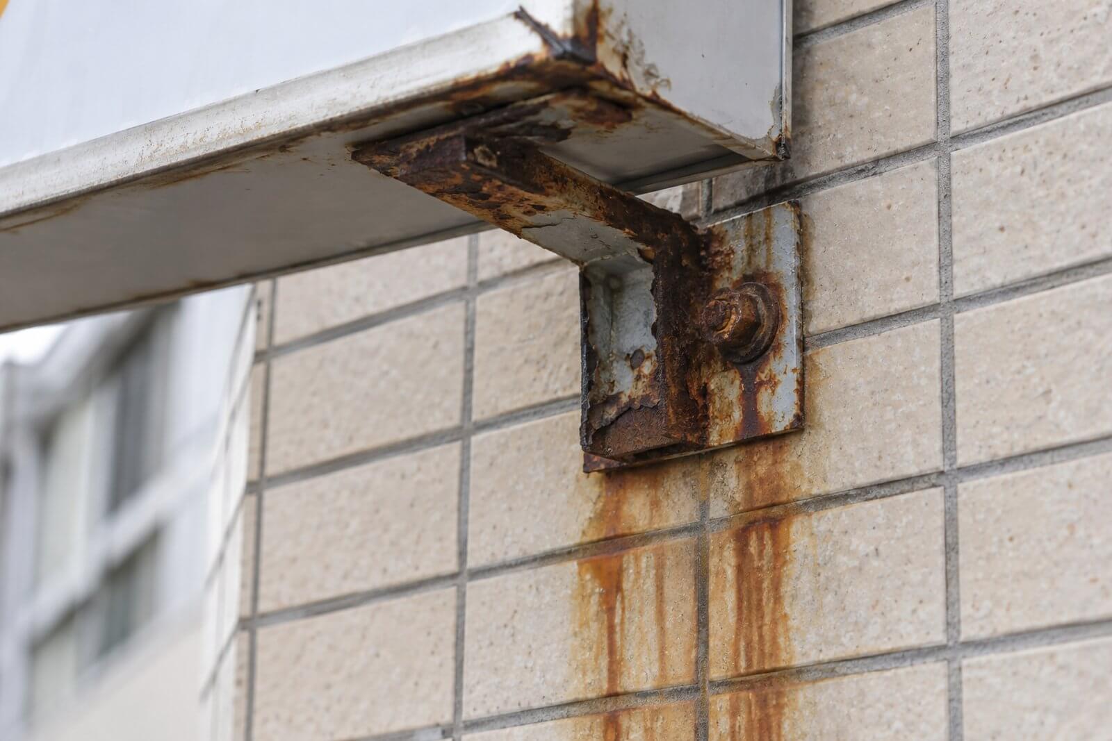 壁面看板の取付金具から外壁に茶色い錆汁が垂れている様子のクローズアップ
