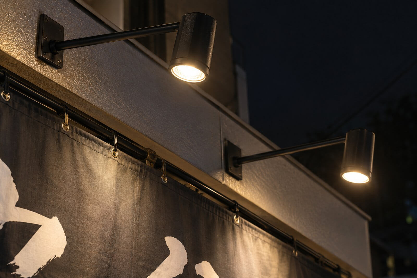 店頭幕の上端を照らす黒いLEDアームスポットライトのアップ