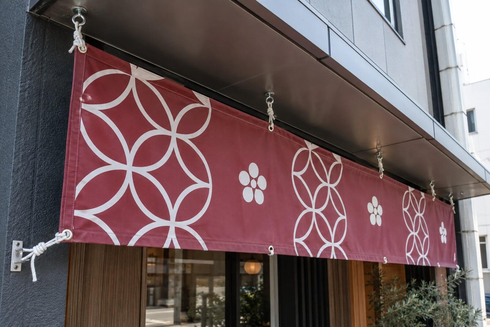 店舗の庇の下にロープで吊り下げた横長の店頭幕
