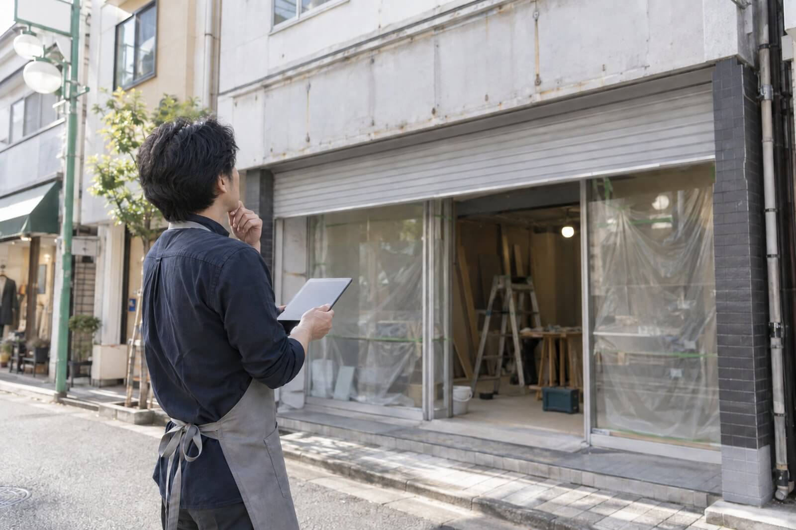 開業準備中の店舗の前でタブレットを見ながら看板を検討する店主