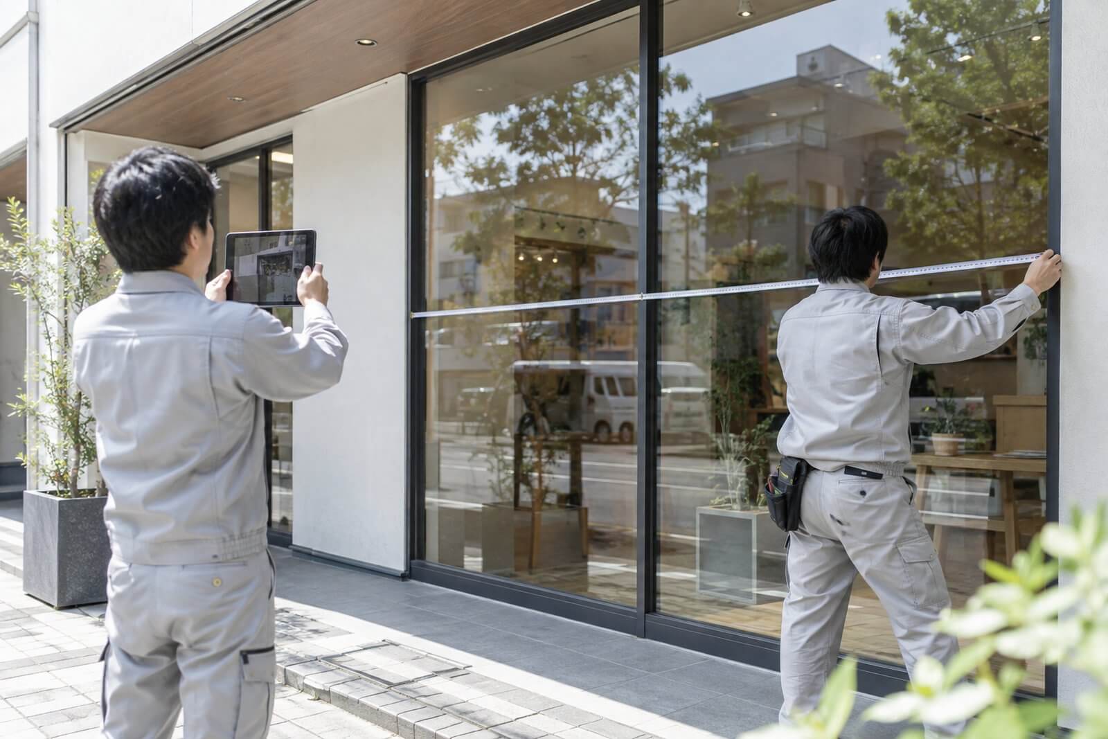 施工スタッフが店舗のガラス面の寸法をメジャーで測り、窓割りを確認している様子