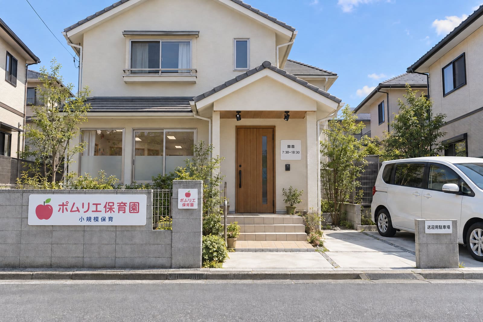 住宅街の2階建ての家を改修した小規模保育園の外観。塀にイラスト入りの園名の看板、門柱に園名のプレート、玄関の横に開園時間の表示、1階の窓の下半分にすりガラス調のフィルム