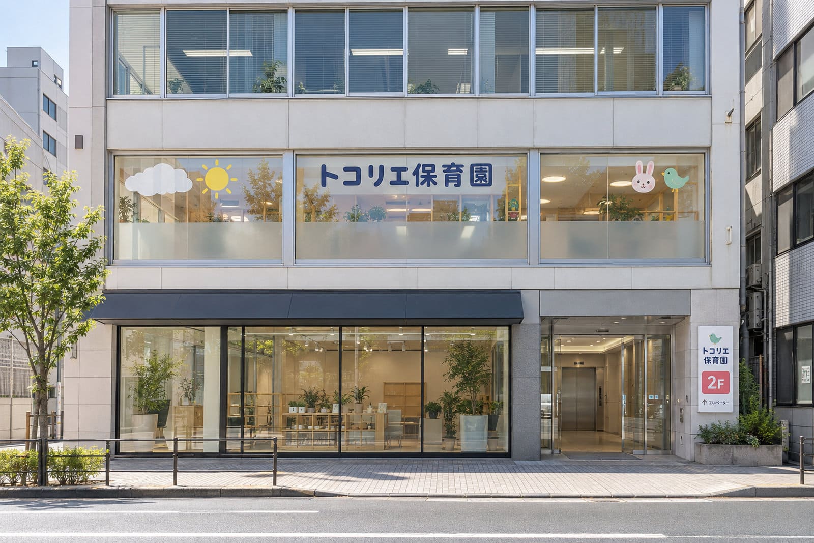 駅前の3階建てのビルの2階にある保育園の外観。2階の窓に園名と小さな雲と太陽のイラスト、1階の入口の横に園名と2Fの案内のプレート