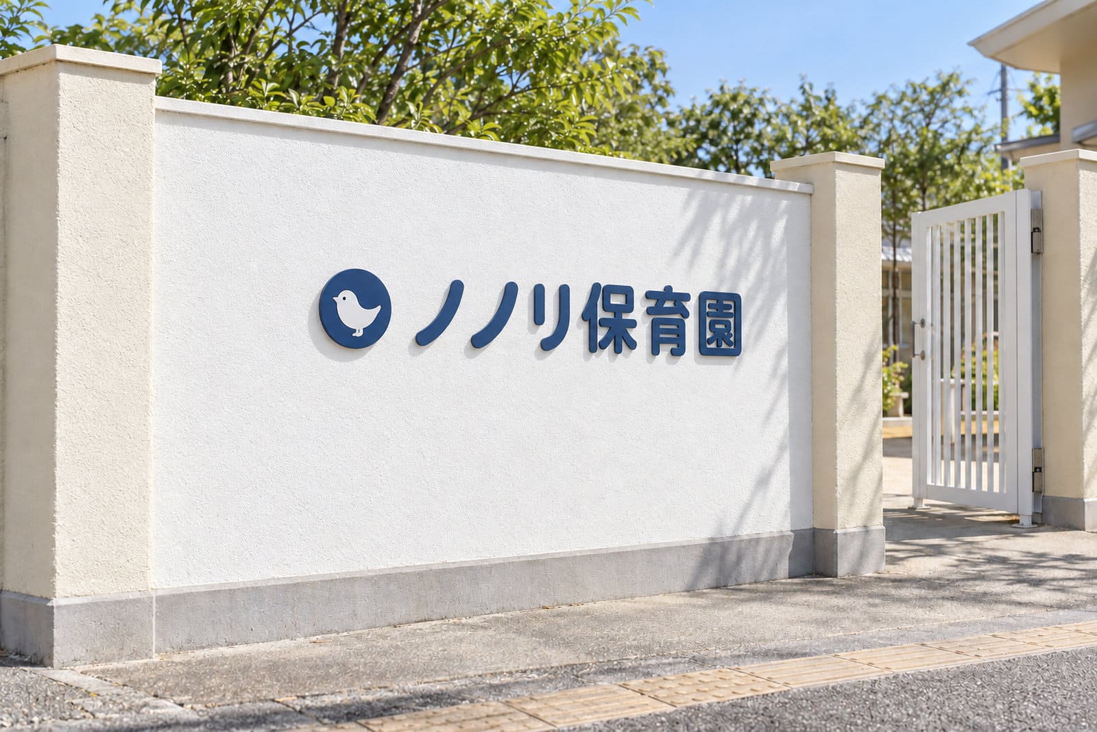 保育園の門の横の白い塀に付けた、くすんだ紺色の文字と小さな丸いロゴだけのシンプルな園名の看板