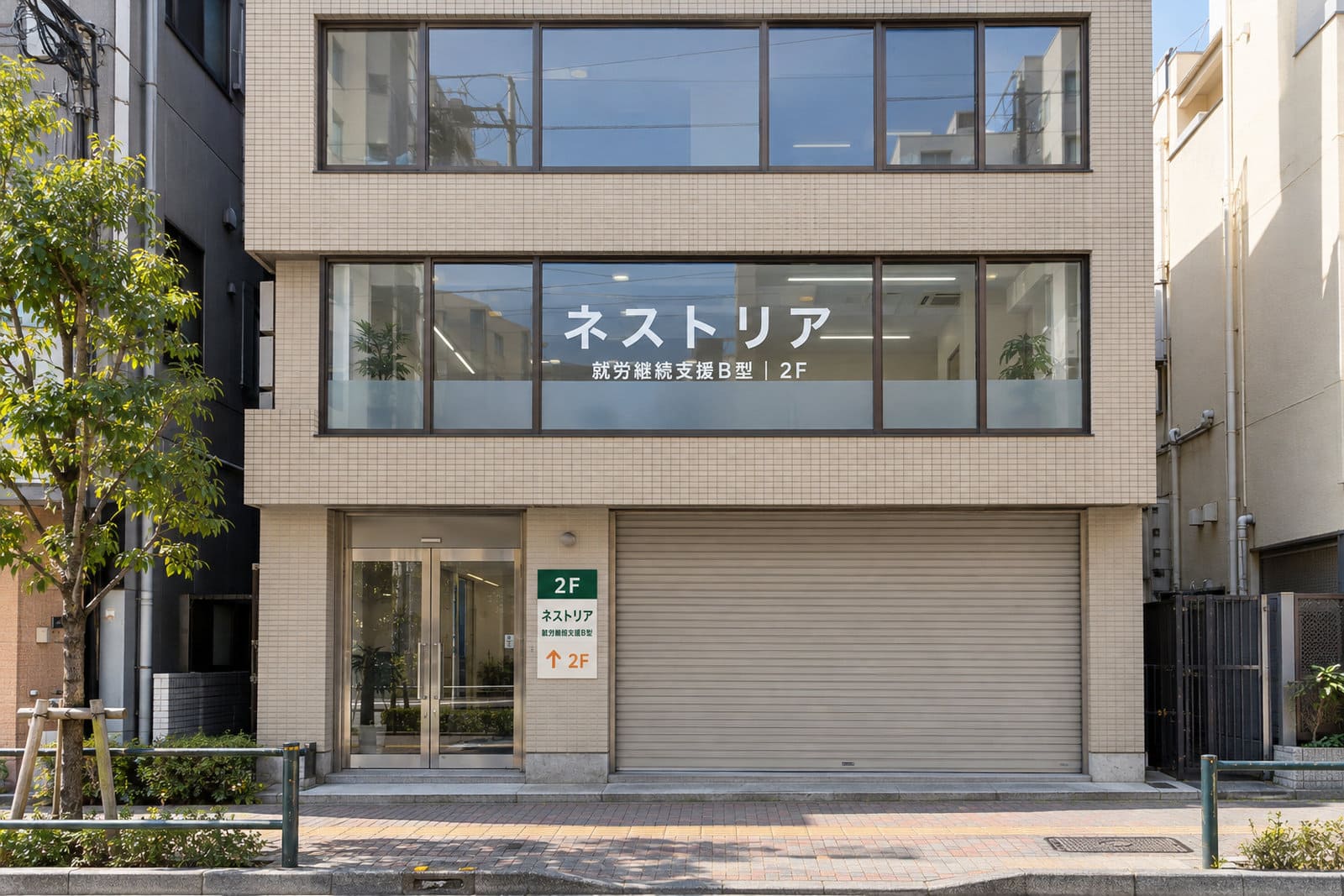 3階建てのビルの2階にある就労支援の事業所の外観。2階の窓に白い文字の施設名、1階の入口の横に施設名と2Fの案内のプレート