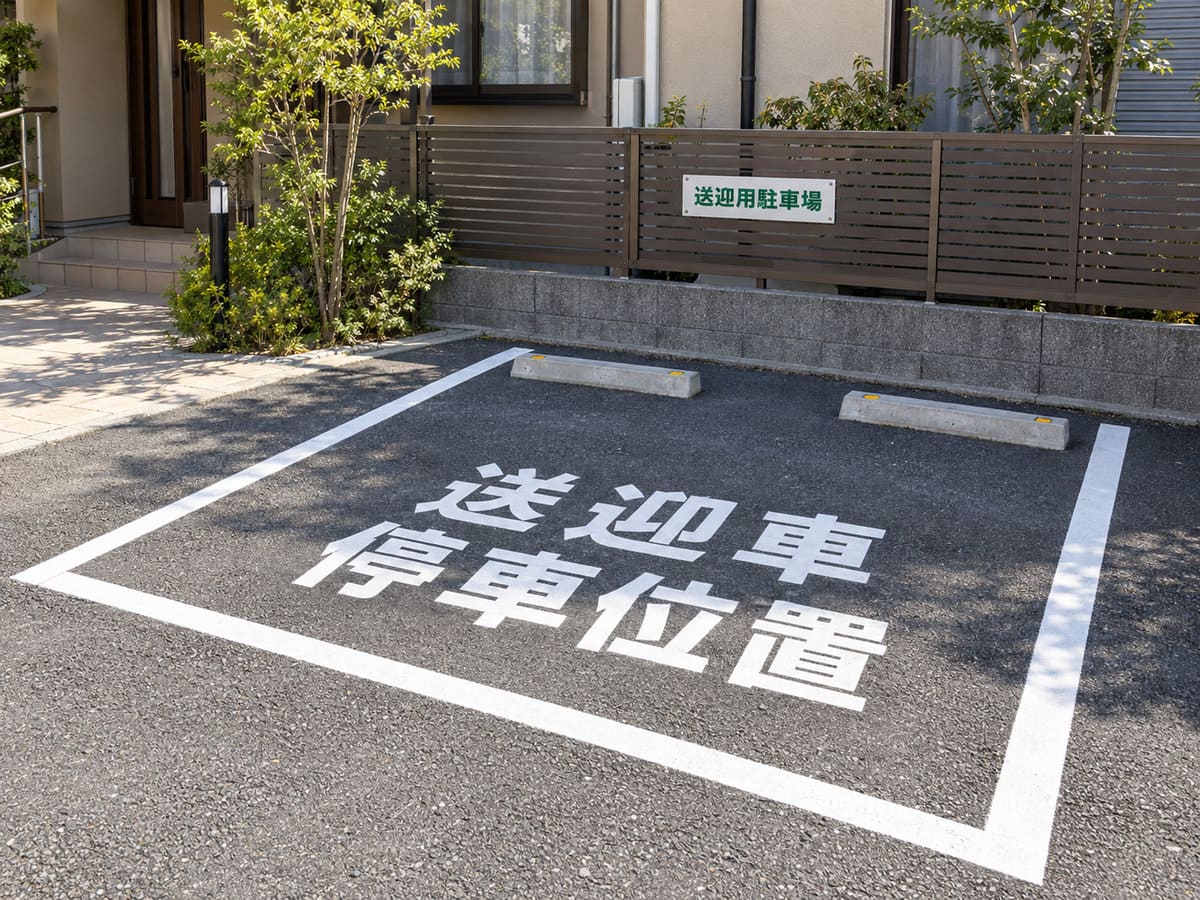 介護施設の駐車場のフェンスに付けた送迎用駐車場のプレートと、路面の停車位置の表示