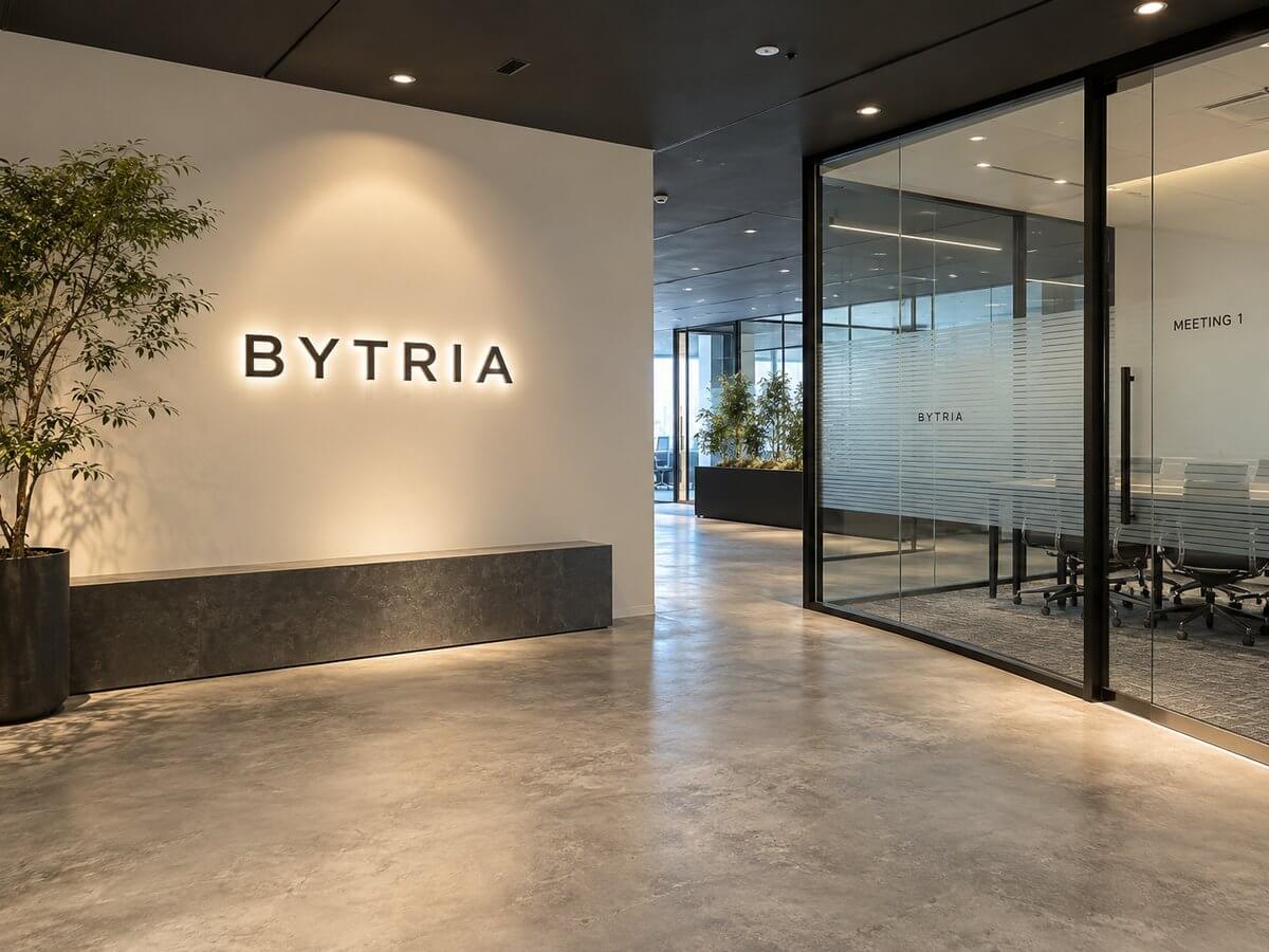 IT企業のエントランス。白い壁に裏側が光るチャンネル文字の社名、会議室のガラスにはストライプのすりガラス調フィルムとロゴ