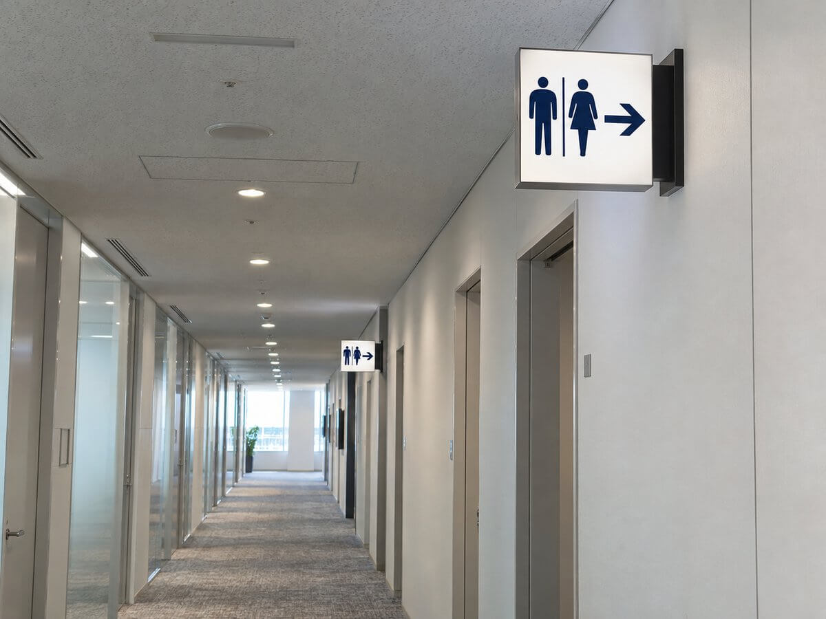 オフィスの長い廊下の壁から突き出して取り付けた両面の案内サイン。トイレと会議室の方向が示されている