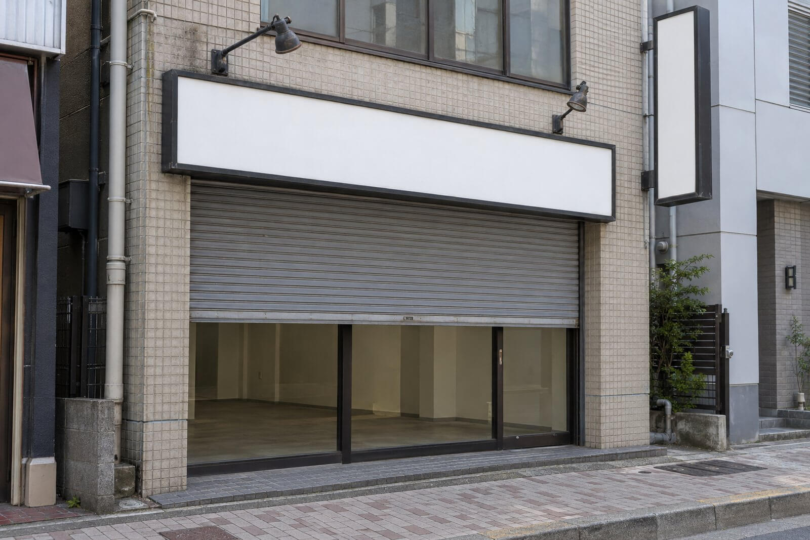空き店舗の入口の上に、前のお店の看板の枠と袖看板が残り、面は白い板でふさがれている