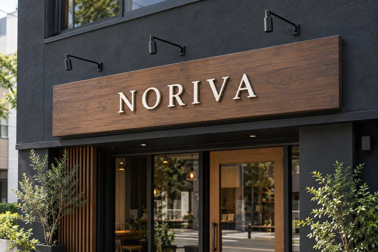 昼の店舗で、黒い外壁と木目の看板の上に黒い本体のアームスポットライトが3灯付き、外観になじんでいる様子
