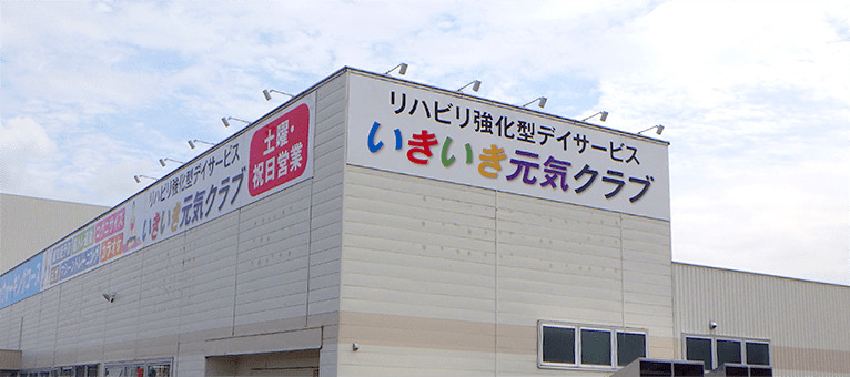 大きな施設の建物の上部にある横長の看板の上に、複数のアームスポットが等間隔に並んで取り付けられている