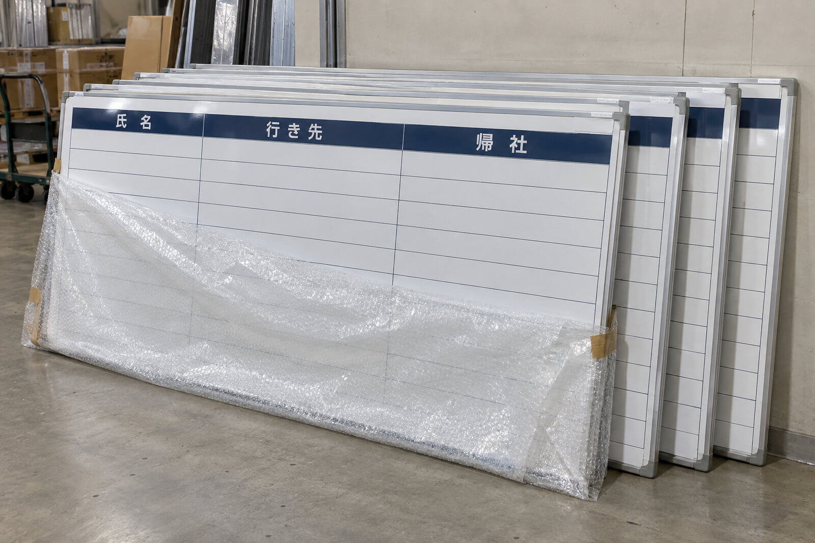 工場の出荷場に、同じデザインの行動予定表を印刷した特注ホワイトボードが5台並んで梱包を待っている様子。それぞれに拠点名のラベルが貼られている